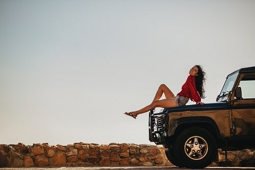 Beautiful woman sitting on car hood