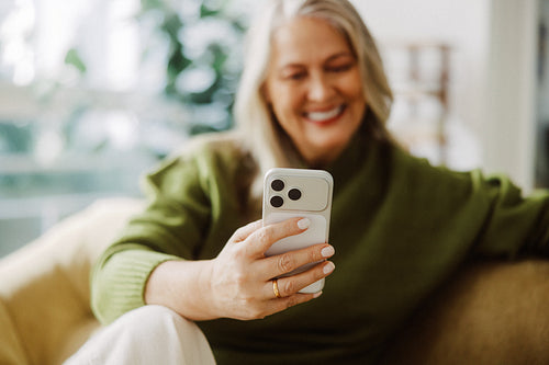 Senior woman uses a smartphone while relaxing at home