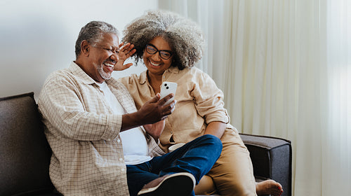 Modern seniors sharing a joyful moment using technology together on a couch