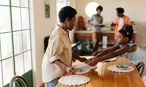 Daughter helping her mom set the table for a family breakfast
