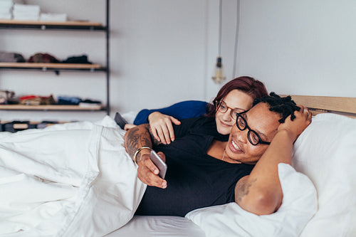 Smiling couple in bed with mobile phone