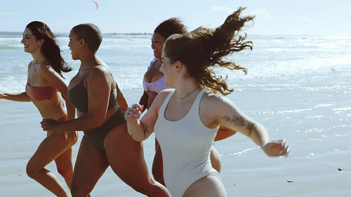Friends in their bikini bodies running on beach