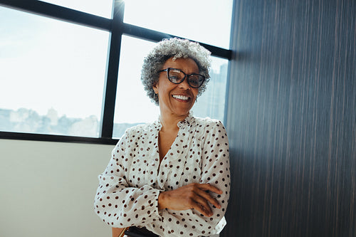 Glasses-wearing woman stands with smile near window in office portrait