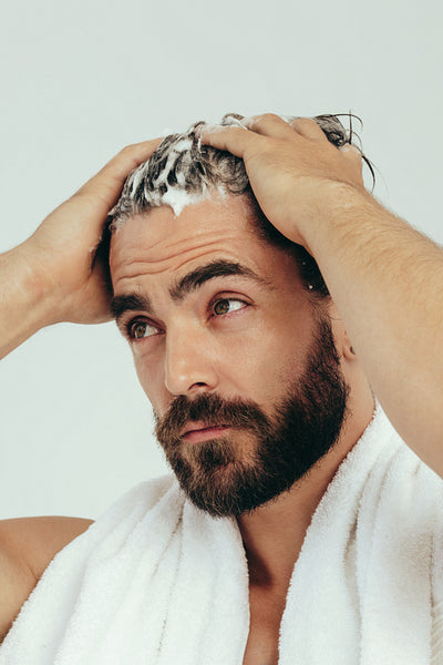 Handsome young man applying shampoo on his hair, preparing for a wash