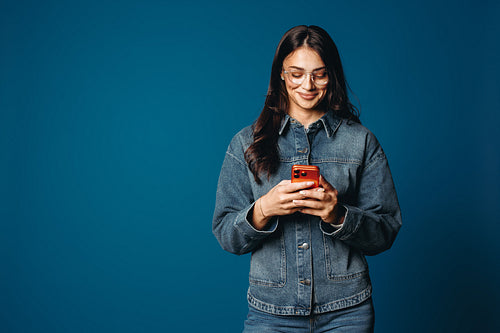 Casual young woman smiling at smartphone in denim jacket studio portrait