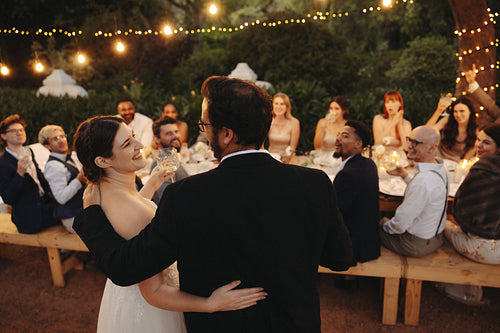 Bride and groom celebrate outdoors with wedding guests under string lights