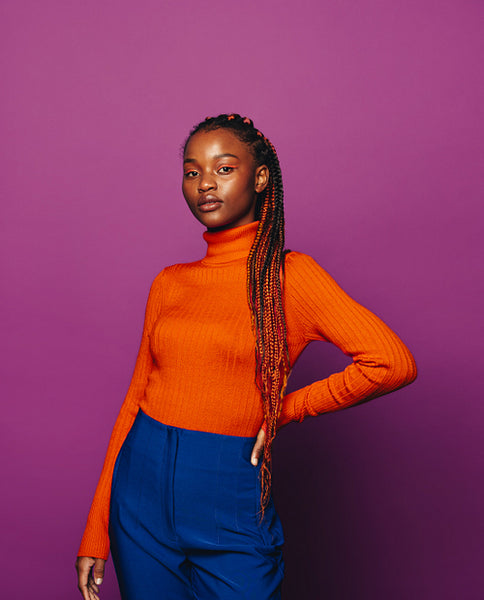 Confident gen z woman with two-tone braids against vibrant purple background.