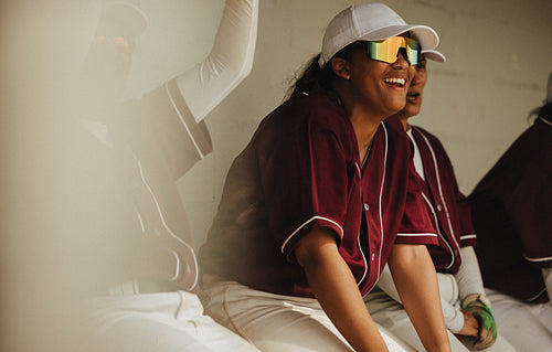 Joyful female baseball player in maroon jersey and cap enjoying a moment in the dugout