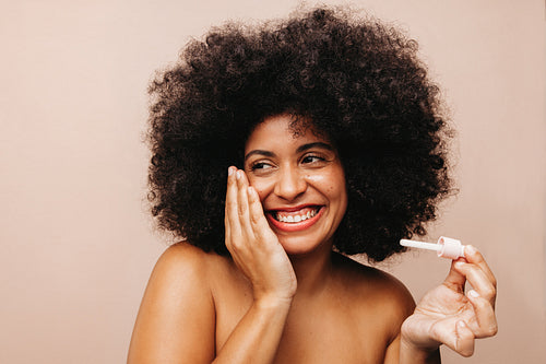 Young woman with Afro hair applying beauty oil on her face