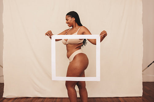 Smiling young woman holding a picture frame in front of her body