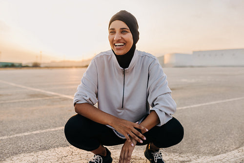 Happy Muslim sportswoman smiling while squatting outdoors