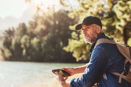 Senior man at a lake with backpack and digital tablet