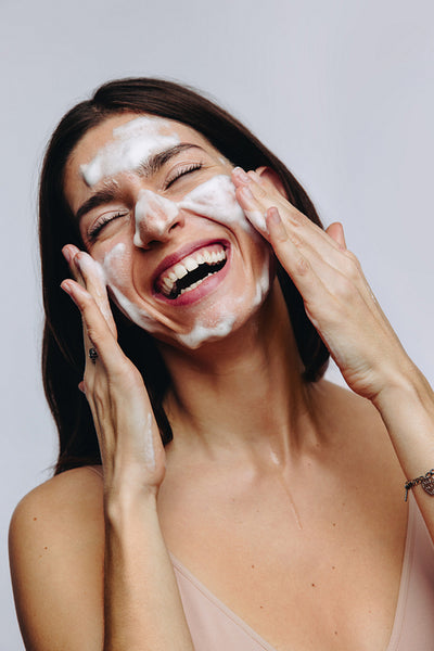 Beautiful woman washing face with foam in studio