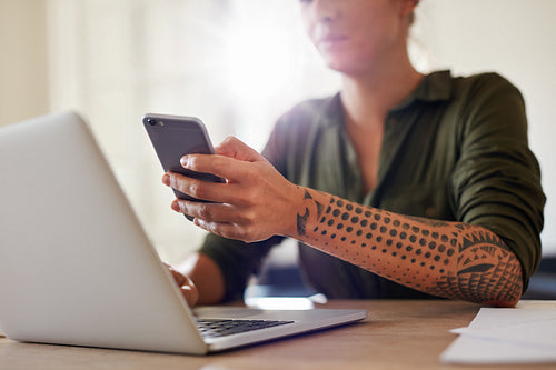 Woman using mobile phone while working on laptop