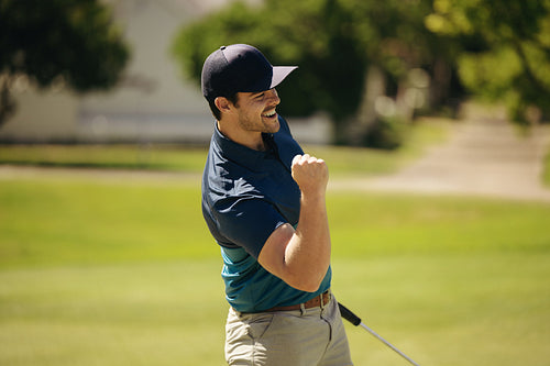 Male golfer celebrating a successful putt with a fist pump and smile
