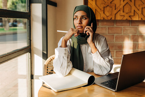 Female student with a hijab making a phone call in a cafe