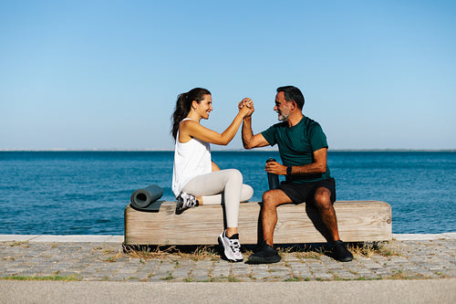 Older man and young woman sharing a handshake on a seaside bench