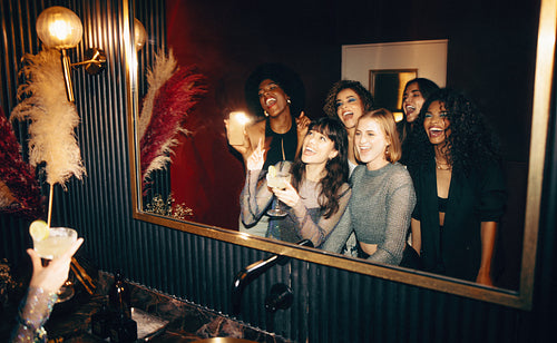Group of young women celebrating together in stylish powder room with a mirror selfie