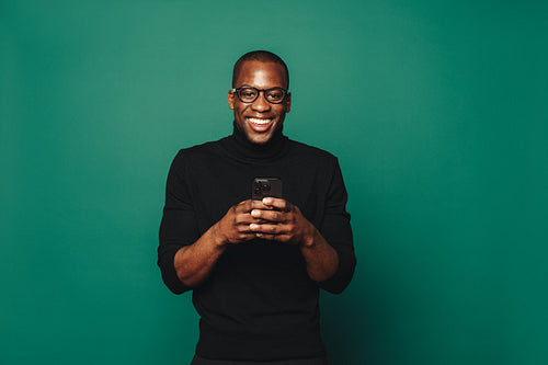 Smiling young man holding a smartphone on a green background