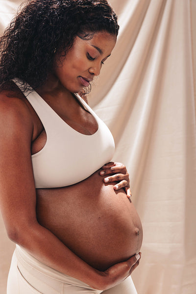 Confident dark-skinned woman hugging her baby bump in studio