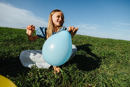 Girl with blue balloon sits on grass