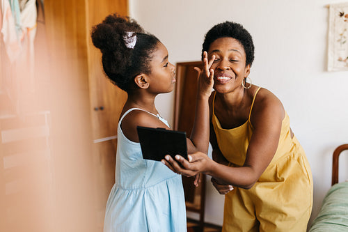 Happy mom getting her makeup done by her daughter at home
