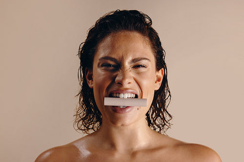 Woman biting unmarked skincare stick with wet hair and glow