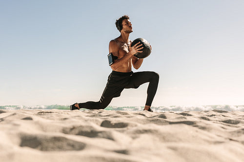 Man training at the beach using a medicine ball