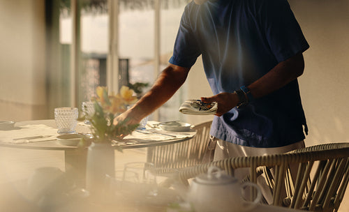 Server setting a breakfast table in a sunny morning with fresh flowers