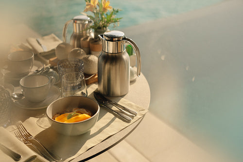 Elegant breakfast set with coffee and fruit by the poolside in a villa on a sunny morning