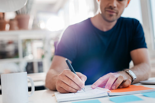 Businessman writing down important notes in diary at his desk