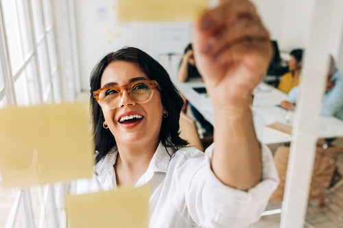 Creative business woman putting sticky notes to a glass wall