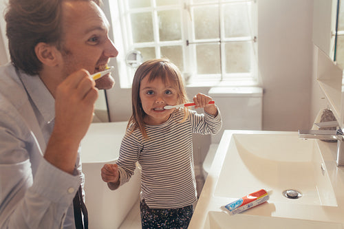 Father teaching daughter how to brush teeth