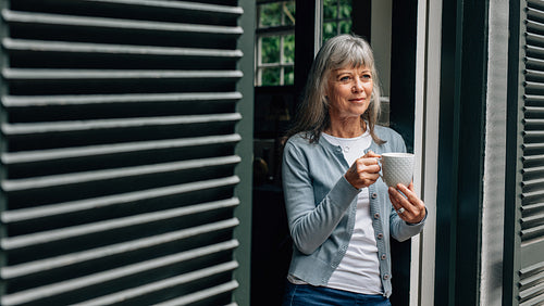 Senior woman standing at the door holding a coffee cup