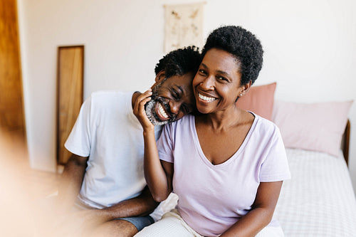 Mature black couple cuddling on bed, laughing and relaxing at home