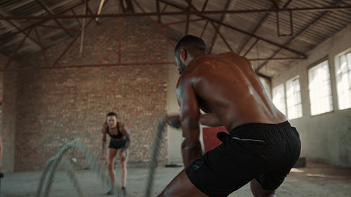 Stong man doing battle rope exercise with personal trainer