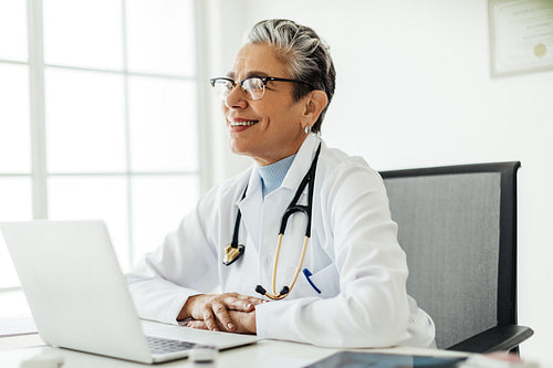 Experienced female doctor sitting at her desk, smiling thoughtfully