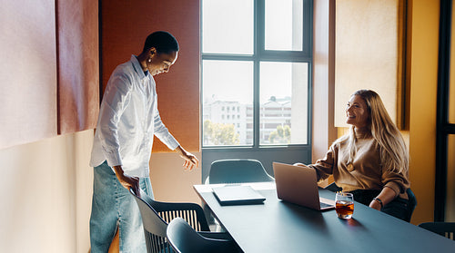Two young professionals discuss ideas in a brightly lit modern office setting