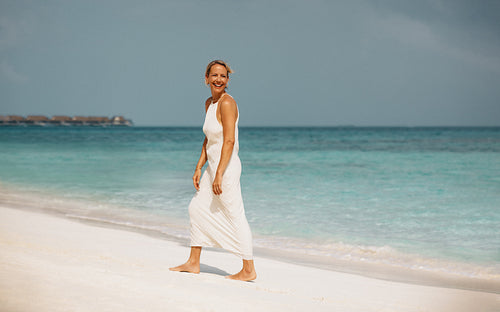 Smiling woman walking on a sunny beach with clear blue waters