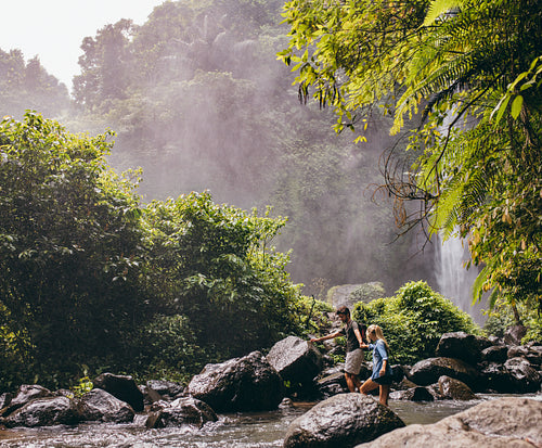 Couple crossing a stream on hike in forest