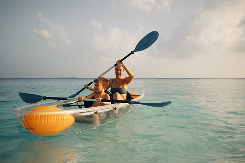 Woman and boy kayaking in clear canoe on a tranquil sea enjoying an outdoor adventure