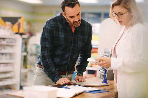 Pharmacist showing medicine to customer in pharmacy