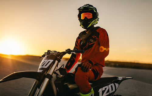 Motocross biker wearing racing gear sitting on his sports bike