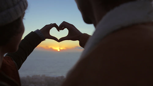 Couple in love looking at sunset with finger heart