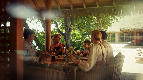 Happy family toasting drinks together during a relaxing meal at a tropical resort villa