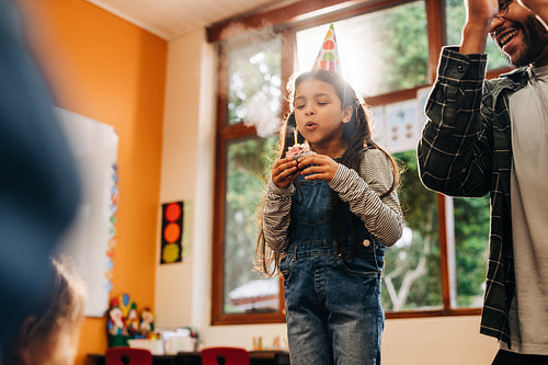 Girl blowing a candle on a cupcake in a classroom. Birthday celebration in elementary school