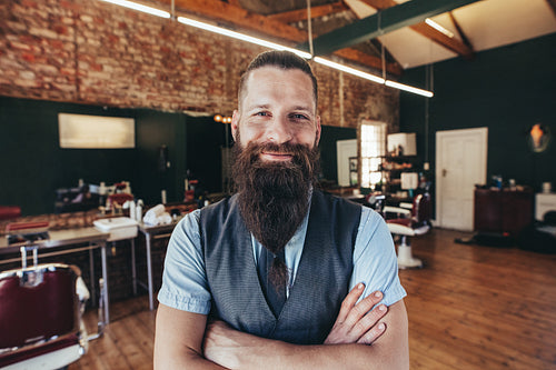 Happy young barber smiling at his barbershop