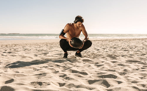 Man training at the beach using a medicine ball listening to music