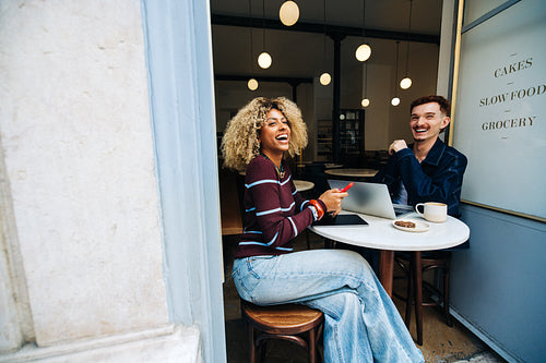 Friends laughing together in a cozy cafe with laptop