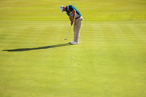 Golfer focuses on short game at golf course on a sunny day, aiming the ball into the hole on putting green